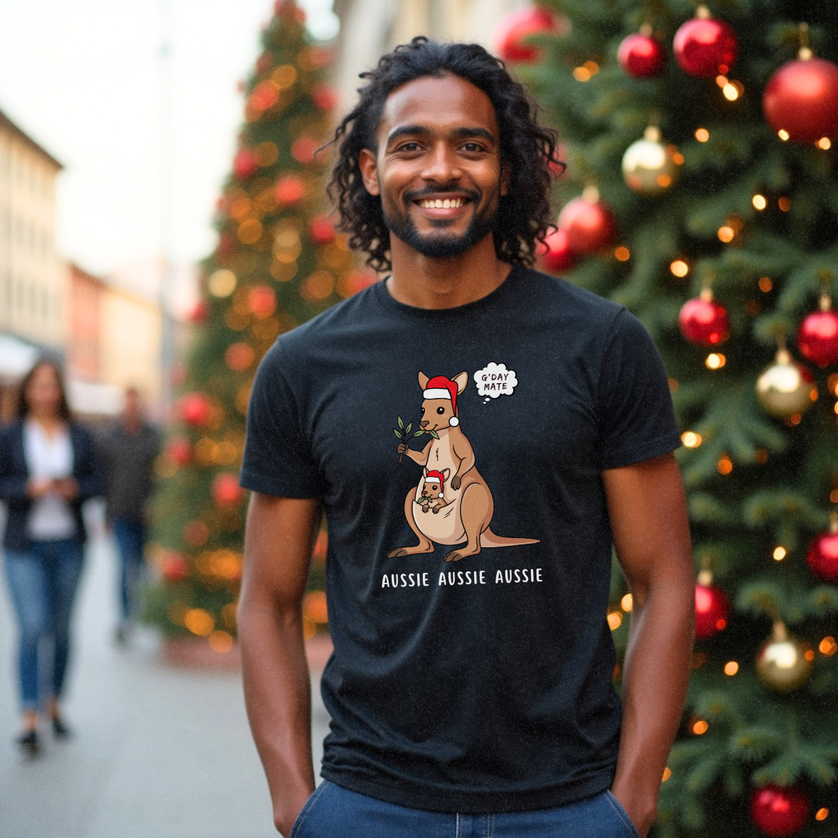 Male in his 30s with short curly black hair standing in front of a Christmas Tree in a street wearing a funny black Christmas t-shirt with a kangaroo and its joey on the front which says 'G'Day Mate Aussie Aussie Aussie' by Faith Looks Good
